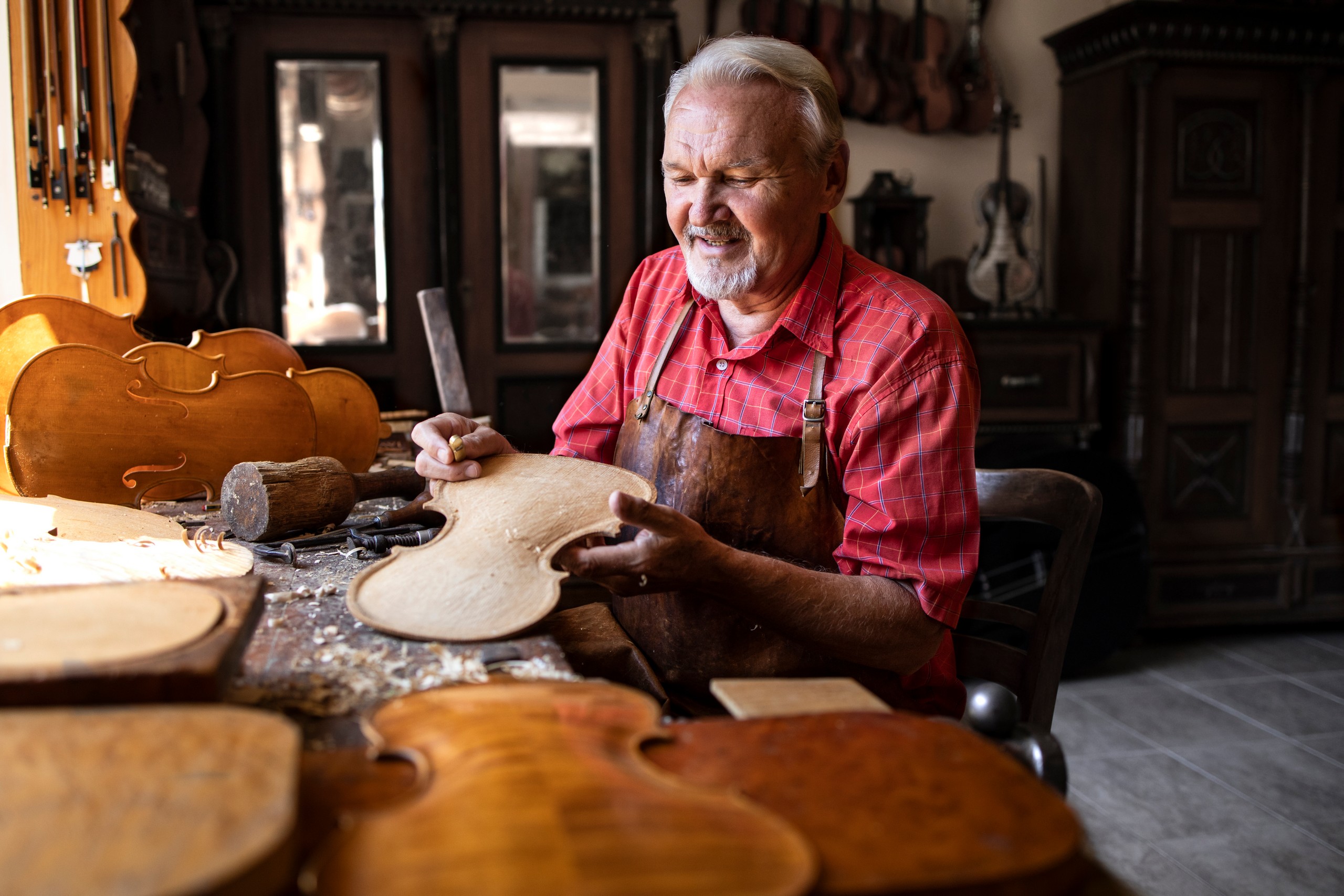 Professional senior carpenter making high quality violin instrument for students of music academy.